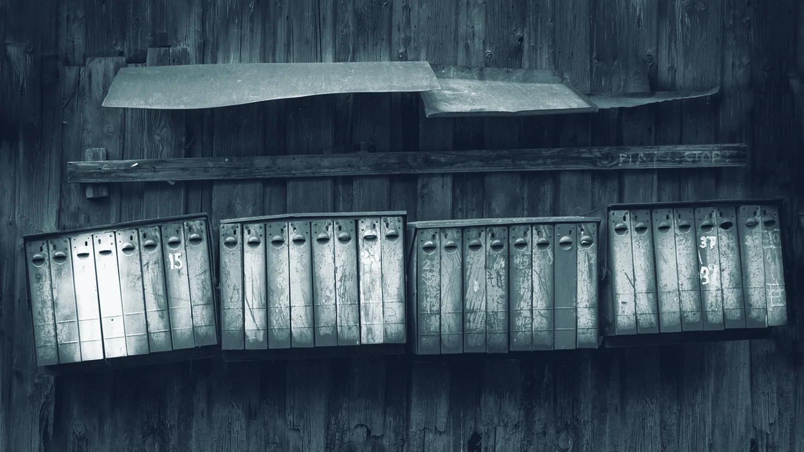Reihe alter Briefkastenfächer an einer verwitterten Holzwand