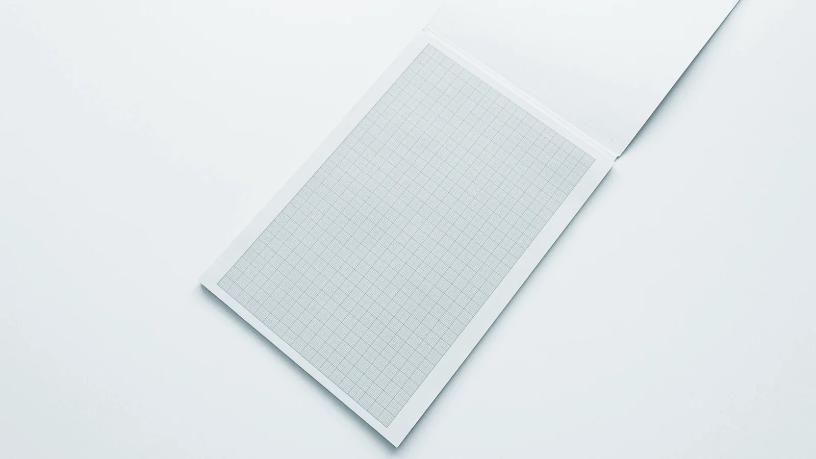 Ein einzelnes Blatt Karopapier liegt schräg auf heller Fläche, eine Ecke steht hoch
