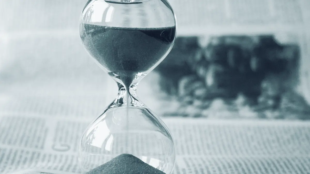 Eine Sanduhr auf einer Zeitungsseite, der Sand ist zur Hälfte durchgelaufen